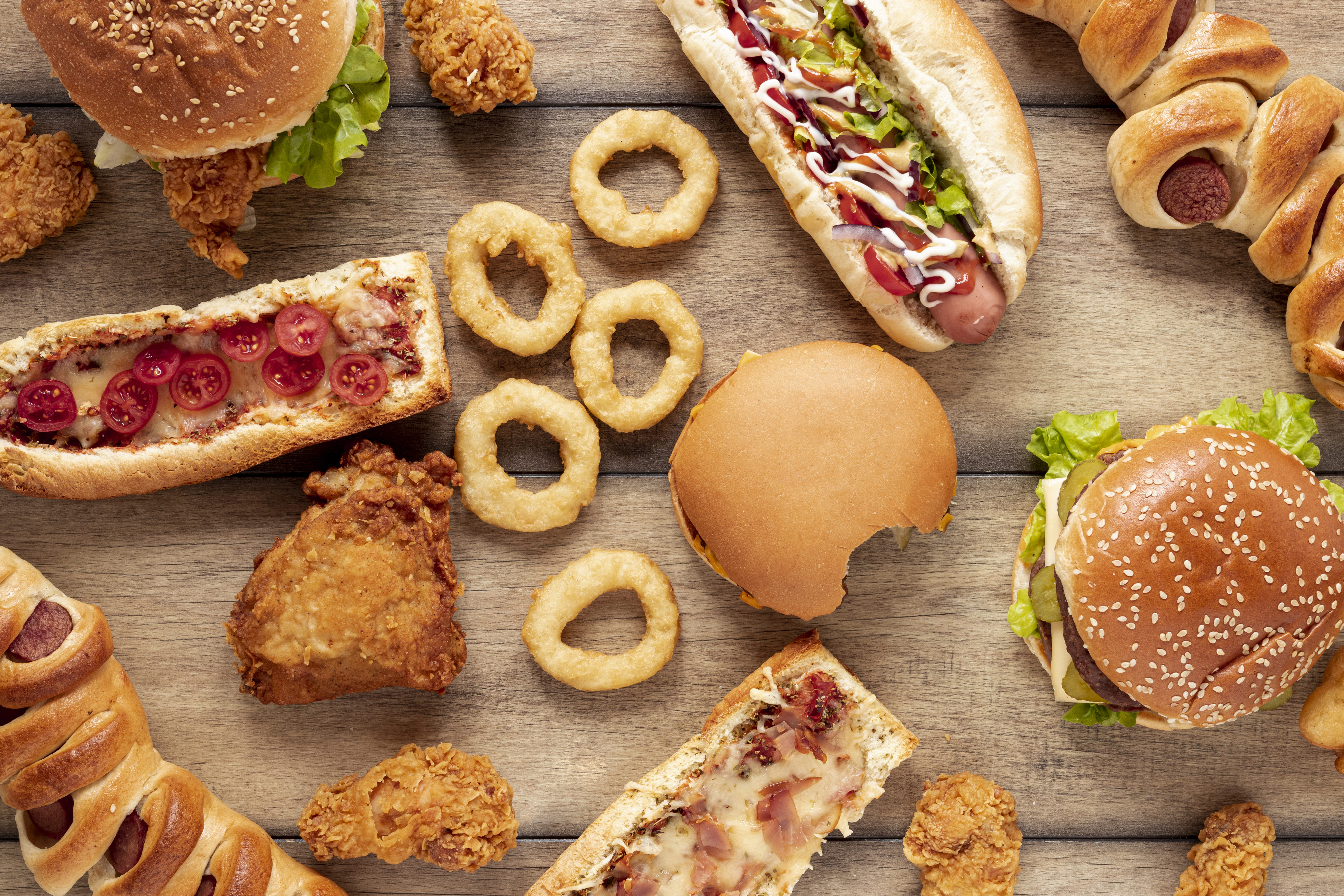 Mesa llena de productos ultraprocesados como hamburguesas, pizzas, pollo frito, hot dogs